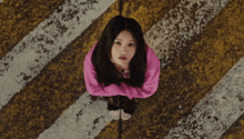 a woman in a pink sweater is standing on a yellow and white striped surface