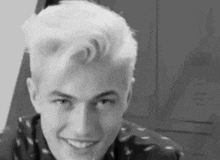 a black and white photo of a young man with white hair smiling and looking at the camera .