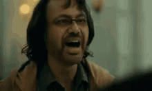 a man with glasses is making a funny face while talking to another man .