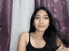 a woman in a black tank top is standing in front of purple curtains