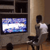 a man sits in a chair watching a basketball game on a flat screen tv