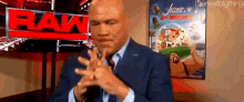 a man in a suit and tie is clapping his hands in front of a raw logo .