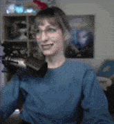 a woman wearing glasses and a blue shirt is sitting in front of a microphone .