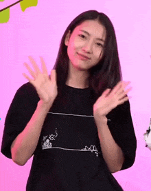 a woman in a black t-shirt is waving her hands and smiling