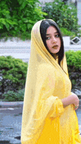 a young woman wearing a yellow dress and a yellow veil is standing in front of a fountain .