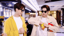 two men wearing sunglasses are standing next to each other and one of them is holding a bag of chips .