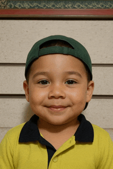 a young boy wearing a green hat and a yellow shirt smiles at the camera