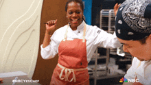 a woman in a pink apron stands next to a man in a bandana with the nbc logo on the bottom