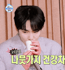 a man in a suit is drinking from a cup with korean writing on the bottom