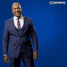 a man in a suit and tie stands in front of a blue background that says fox deportes on it