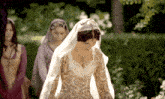 a woman in a white dress with a veil on her head stands in a garden