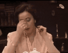 a woman is sitting at a table with a cup of tea in her hand and covering her face with her hand .