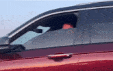 a man is sitting in the driver 's seat of a red car .