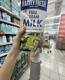 a person holding a carton of harvey fresh full cream milk in a store