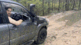 a man is driving a car on a muddy road with his arm out the window .