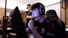 a man wearing headphones and a blacklyte gaming chair looks at a computer screen