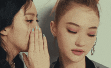 a woman whispering into another woman 's ear with her hand