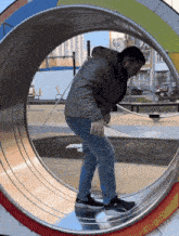 a man is walking through a metal tube in a park while wearing a gray jacket