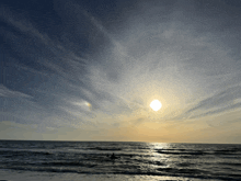 the sun is setting over the ocean with a few clouds