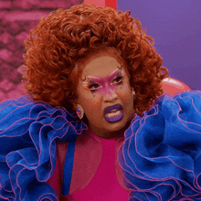 a drag queen wearing a pink top and blue ruffled sleeves