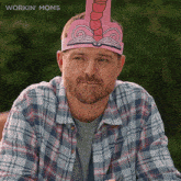 a man in a plaid shirt is wearing a pink paper hat that looks like a book