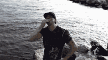 a man is standing in front of a body of water and covering his nose .