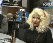 a woman with blonde hair is talking into a microphone in front of a sign that says power 105.1