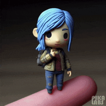 a figurine of a girl with blue hair is sitting on a pink finger with pika labs written on it