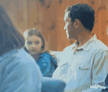 a man in a white shirt is talking to a girl in a blue shirt while another woman looks on