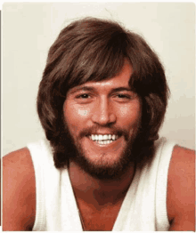 a man with a beard and a white tank top smiles for the camera