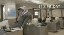 a man in a suit and tie is jumping over a desk with the words it 's friday written above him