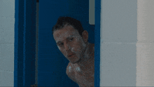 a shirtless man with soap on his face looks out of a doorway