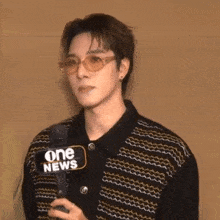 a young man wearing sunglasses and a one news microphone