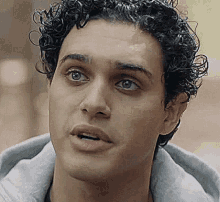 a close up of a man 's face with curly hair and a gray hoodie .