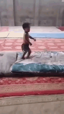 a young boy is jumping on a mattress on a red rug .