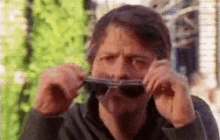 a man is holding a pair of sunglasses in front of his face .