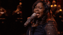 a woman is singing into a microphone in front of a choir