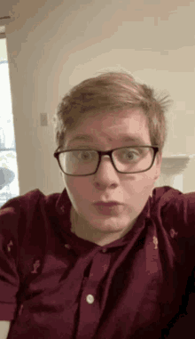 a young man wearing glasses and a maroon shirt looks surprised