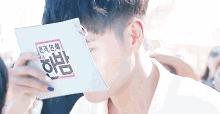 a young man is covering his face with a piece of paper while reading a book .