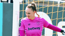 a female soccer goalkeeper in a pink jersey is standing in front of a goal .