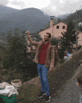 a man in a brown jacket holds up a bottle in front of a house