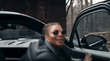 a woman wearing sunglasses and a black jacket is getting out of a car