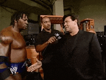 a man in a black suit is talking to a wrestler in a wrestling outfit