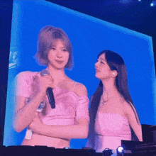 a woman in a pink top is holding a microphone while another woman looks on