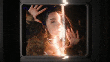 a woman in a fur coat is behind a glass with her hands up