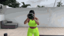 a woman in a neon yellow outfit is holding a large black ball in front of her face