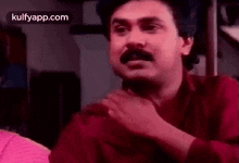 a man with a mustache is making a funny face while sitting in a room .
