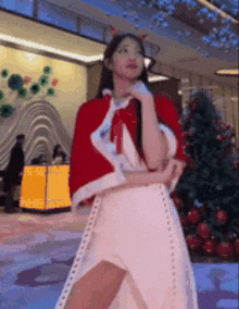a woman is wearing a santa claus costume and standing in front of a christmas tree .