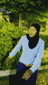 a woman wearing a hijab and a blue shirt is standing in front of trees