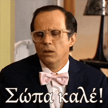 a man wearing glasses and a pink bow tie has a caption in a foreign language that says σαπα καλε